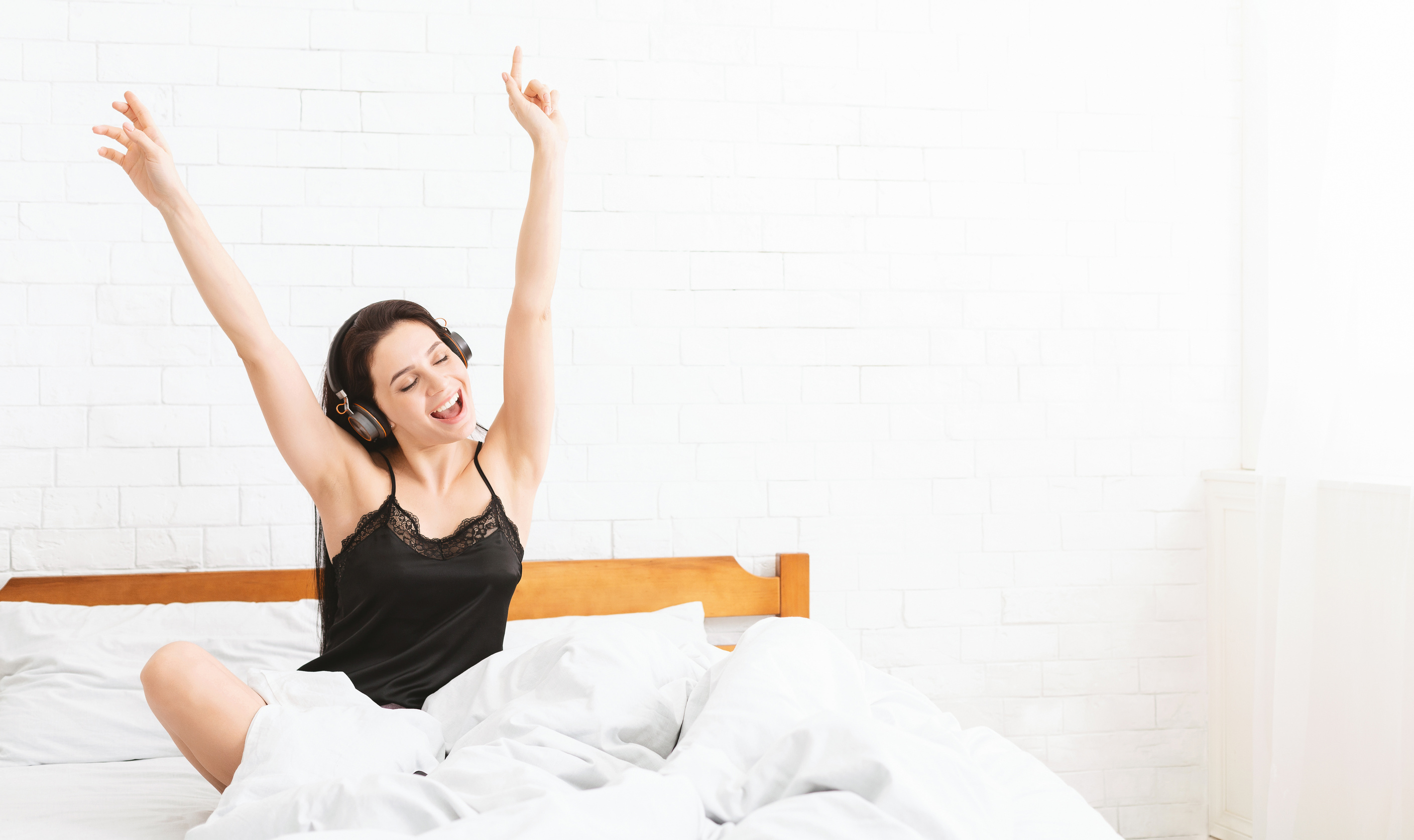 Energetic woman dancing in bed, listening to music